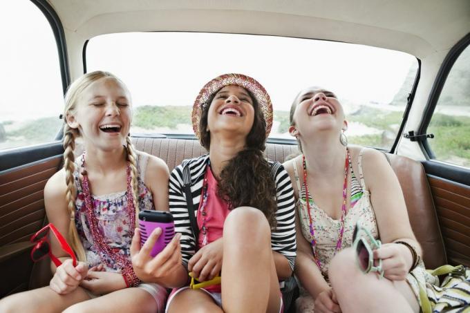 három lány nevet egy jármű hátsó ülésén