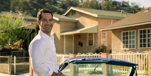 Manuel Garcia Rulfo mint Mickey Haller a Lincoln Lawyer 2. évadában mosolyogva, ahogy a vintage kék lincoln kabrió mellett áll