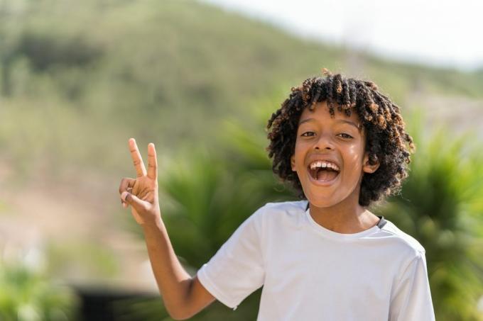 10 éves afro-amerikai fiú hangosan nevet, miközben a béke jelét készíti