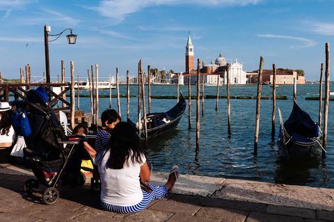 A turisták a földön ülnek Velencében, miközben a San Giorgio templomot nézik