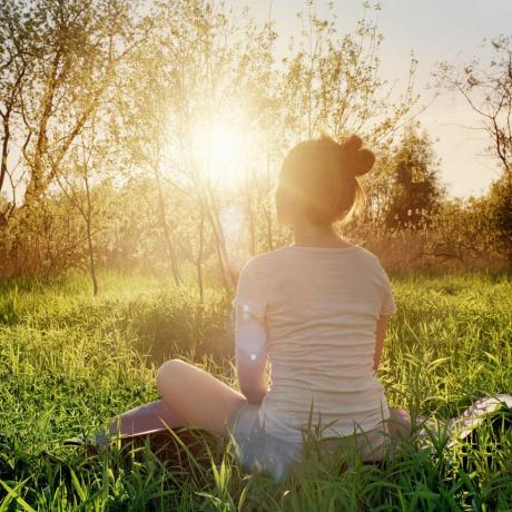 fiatal nő ül jóga helyzetben élvezi a naplementét a természetben