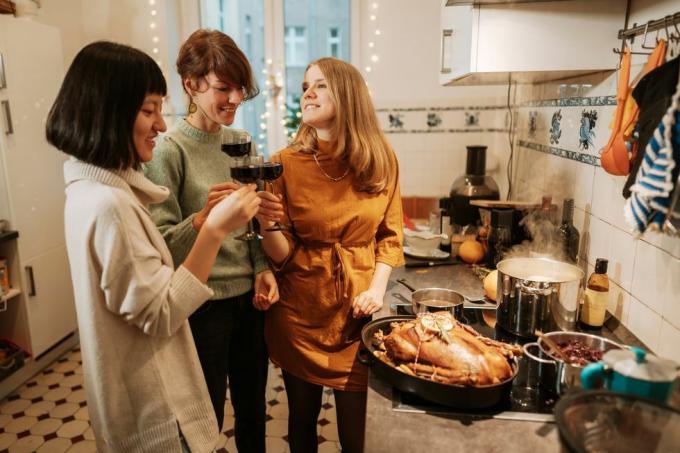 három nő vörösbort iszik, miközben pulyka ételt készít otthon, egy pulyka és három fazék a tűzhelyen főz